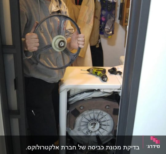 אדם מחזיק גלגל מכונת כביסה, מברגה על המכונה